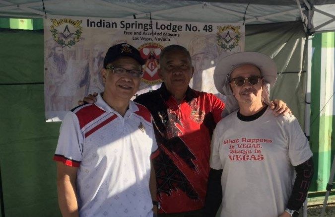 Three members stand arm in arm under a canopy in front of an Indian Springs Lodge No. 48 banner at an outdoor event.